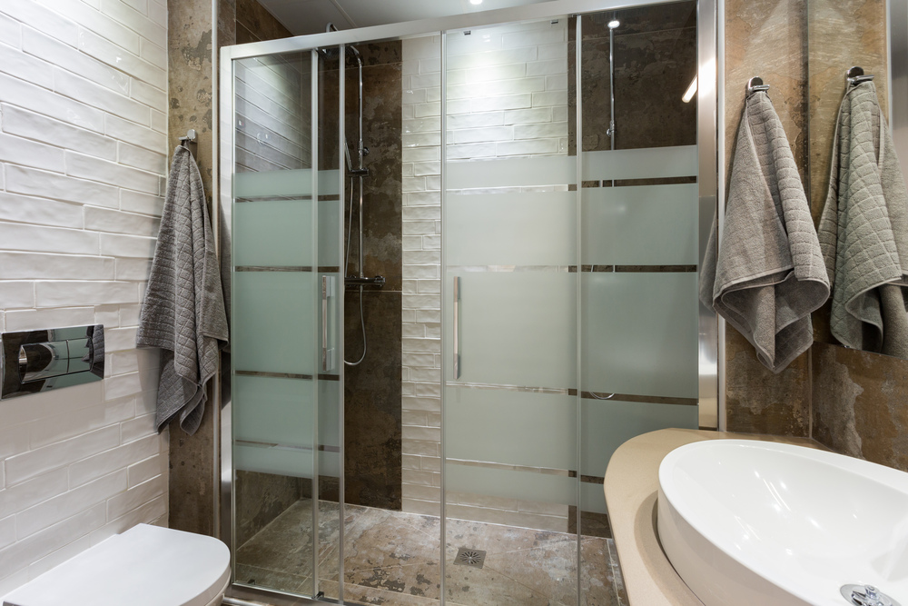 Baño elegante con mampara de vidrio templado, ideal para evitar salpicaduras, junto con accesorios funcionales que optimizan el espacio y la comodidad.